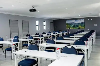an empty classroom with white tables and blue chairs at Khayalami Hotel - Secunda in Secunda