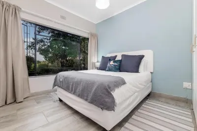 a white bedroom with a bed and a window at Honeysuckle in Tzaneen