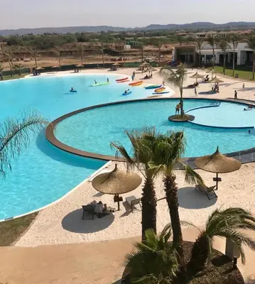 a large swimming pool with palm trees and umbrellas at 2 Bedroom The Blyde Crystal Lagoon Luxe in Pretoria