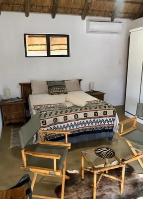 a bedroom with a bed and chairs in a room at NIANI HYENA chalet in Hoedspruit