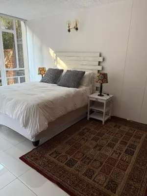 a white bedroom with a bed and a window at Cosy flat with garden near Loftus & embassies in Pretoria