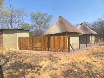 two huts with thatched roofs and a wooden fence at Vlakvark Tented Camp in Bela-Bela