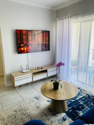 a living room with a table and a tv on the wall at The Blyde Taffys Place in Pretoria