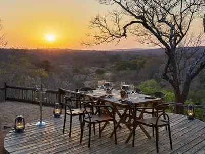 a table and chairs on a wooden deck with the sunset at Toro River by Newmark in Makalali Game Reserve