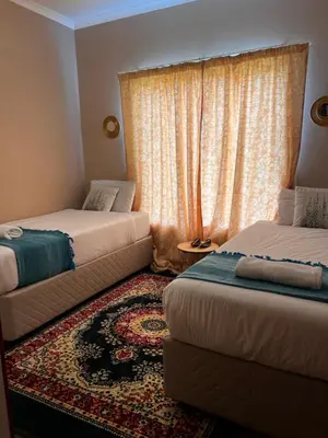 a room with two beds and a window with a rug at Royal Apartments in Burgersfort