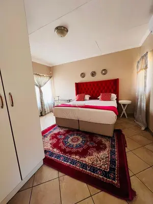 a bedroom with a bed with a red headboard and a rug at Royal Apartments in Burgersfort