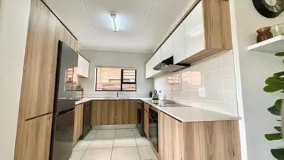a kitchen with white walls and wooden cabinets at The Blyde - Lagoon Facing 3 Bedroom apartment in Pretoria