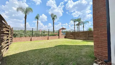 a backyard with palm trees and a brick fence at The Blyde - Lagoon Facing 3 Bedroom apartment in Pretoria