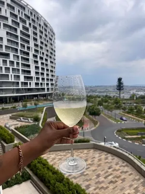 a person holding a glass of wine in front of a building at Mphoentle Residence ellipse waterfall in Midrand