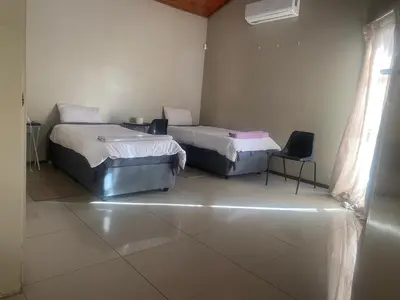 a room with two beds and a chair in it at Mbobo Legacy Residence in Pretoria