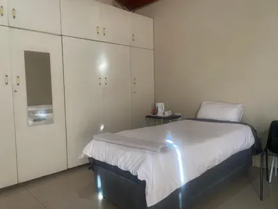 a bedroom with a bed with white walls and cabinets at Mbobo Legacy Residence in Pretoria