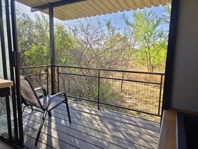 a balcony with a chair and a view of the woods at Hot Tub Haven - Modimolle in Modimolle