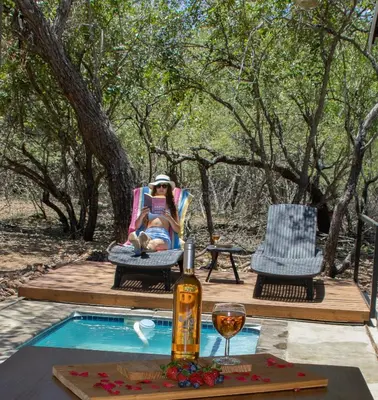 a woman sitting in a chair at a table with a bottle of wine at Ratel Katel in Marloth Park