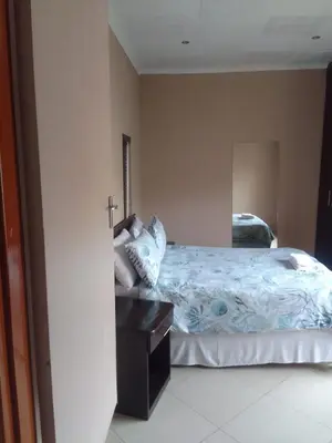 a bedroom with a bed with a dresser and a mirror at Nomanini Guesthouse in Nelspruit
