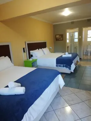 a hotel room with two beds with blue and white sheets at Amigos Bed & Breakfast - No loadshedding in Nelspruit