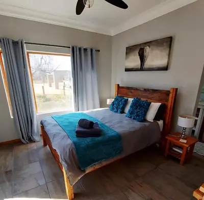 a bedroom with a bed with blue pillows and a window at Oryx Lodge in Brits