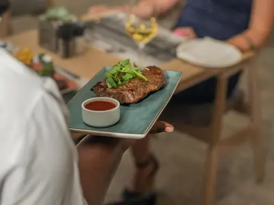 a person holding a plate with a steak and sauce at ANEW Resort Hazyview Kruger Park in Hazyview