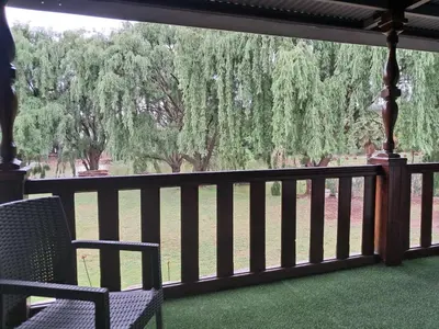 a porch with two chairs and a view of trees at The Nugget Guest Lodge in Kempton Park