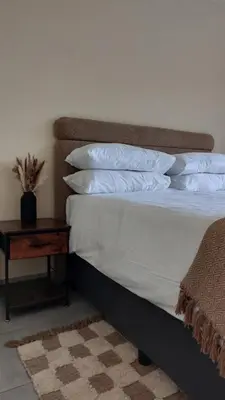 a bed with white pillows and a table with a plant on it at La Boheme in Pretoria