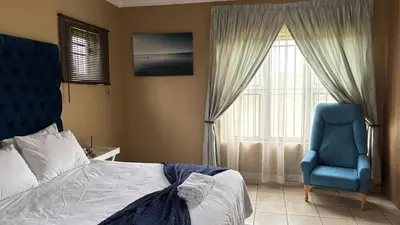 a bedroom with a bed and a blue chair and a window at The N1 Farm Place in Pretoria