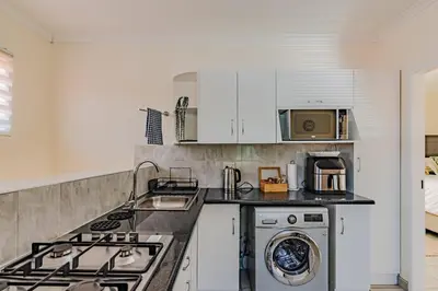 a kitchen with white cabinets and a washer and dryer at Upstairs at 47 in Centurion