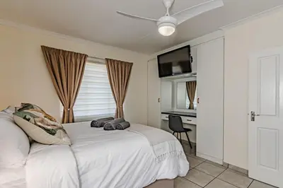 a bedroom with a bed with a ceiling fan and a desk at Upstairs at 47 in Centurion