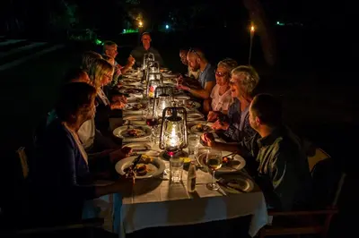 a group of people sitting at a long table at night at Honeyguide Tented Safari Camp - Khoka Moya in Manyeleti Game Reserve