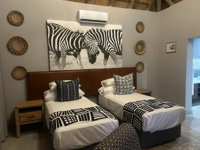 two beds in a room with a painting of zebras at Cheetah Paw Safari Lodge in Guernsey Nature Reserve