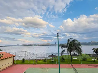 a tennis court next to a lake with a palm tree at Olives by Agnes 31 in Hartbeespoort