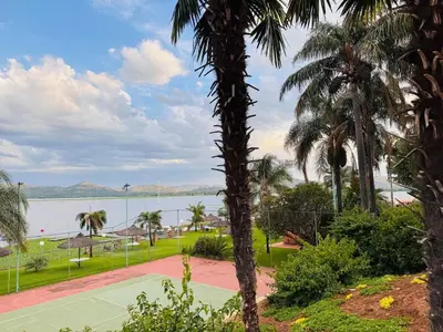a tennis court next to a body of water with palm trees at Olives by Agnes 31 in Hartbeespoort