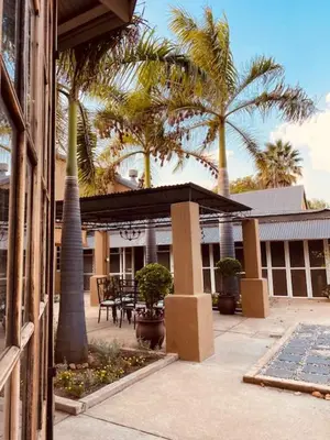 a patio with palm trees and a building with a table at Old Mine Guesthouse in Musina