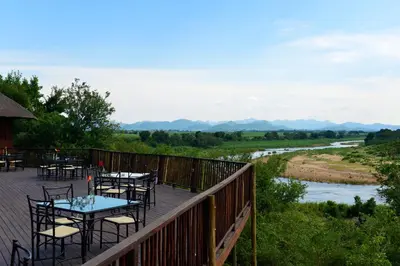 a deck with tables and chairs overlooking a river at Pestana Kruger Lodge in Malelane