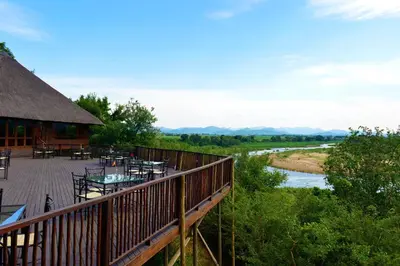 a deck with tables and chairs next to a river at Pestana Kruger Lodge in Malelane