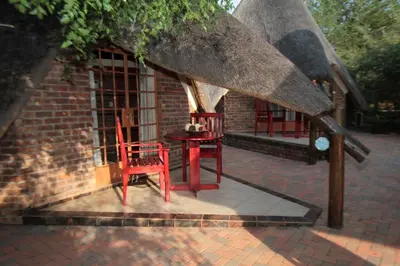 two red chairs and a table in front of a building at Big Tuskers Bush Camp in Marloth Park