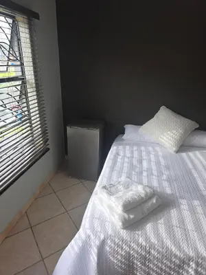 a bedroom with a bed with white sheets and a window at The Good Samaritan 2 in Witbank