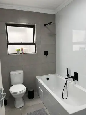 a bathroom with a toilet and a tub and a window at Condo in Sunninghill, Sandton in Sandton