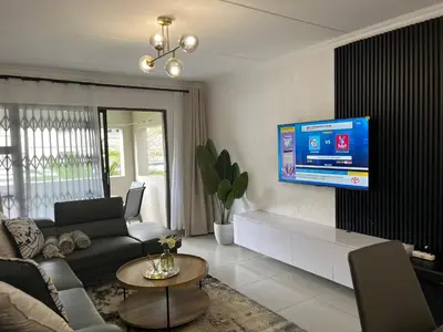 a living room with a couch and a tv on a wall at Condo in Sunninghill, Sandton in Sandton