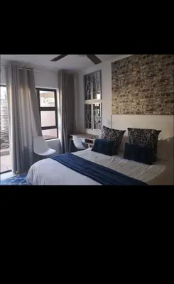 a bedroom with a king sized bed with a brick wall at Soteria House in Kempton Park