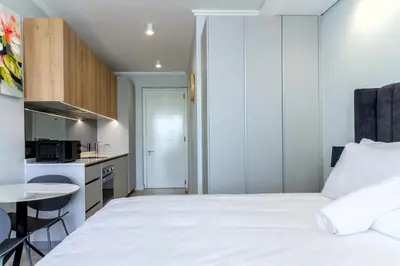 a bedroom with a white bed and a kitchen at Ellipse Waterfall 4212 in Midrand