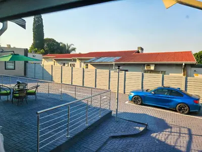 a blue car parked in a parking lot next to a fence at The M GuestHouse in Kempton Park