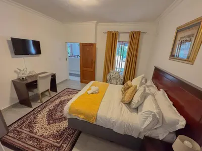 a bedroom with a bed and a desk and a television at Miyanwe Guest House - Waterkloof in Pretoria
