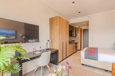 a bedroom with a bed and a desk and a kitchen at Menlyn Maine in Pretoria