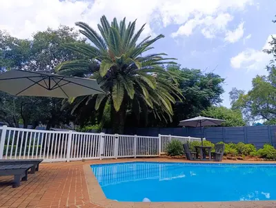 a pool with a white fence and a palm tree and an umbrella at Joy Haven - Cottage in Centurion