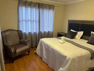 a bedroom with a bed and a chair and a window at Peshi's Guest House in Pretoria