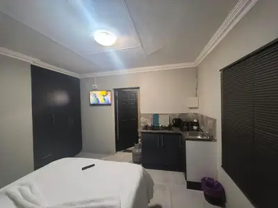 a bedroom with a white bed and a kitchen at The Good Samaritan 1 in Witbank