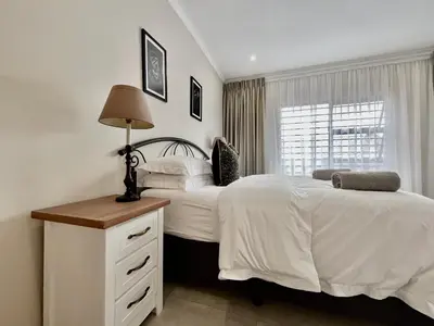a bedroom with two beds and a lamp and a window at Modern 2 Bedroom Apartment near Carstenhof Hospital, Glen Austin in Midrand