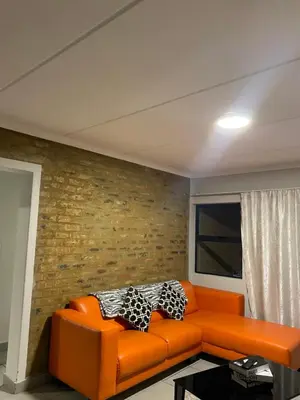an orange couch in a room with a brick wall at Unmatched Stays in Kempton Park