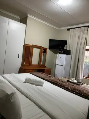 a bedroom with a white bed and a refrigerator at Kloofyard Guesthouse in Pretoria