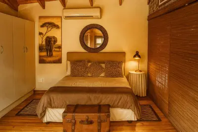 a bedroom with a bed with a mirror and a suitcase at Tree Lodge by My Adventure House in Marloth Park