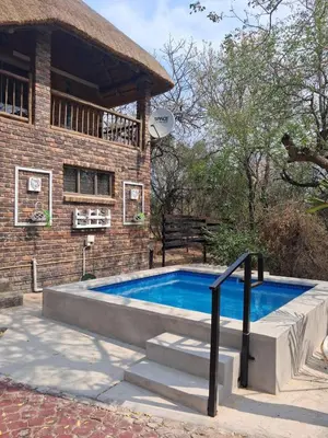 a swimming pool in front of a brick building at Figtree Escape in Marloth Park